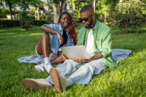 Calm African American couple sits under trees, studying online. Man browses exam resources on gadget